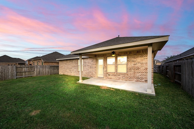 back house at dusk with a yard and a patio area