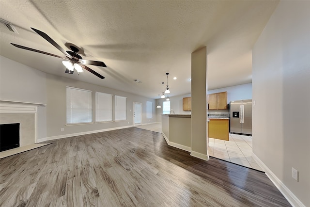 unfurnished living room with ceiling fan, a premium fireplace, a textured ceiling, and light hardwood / wood-style flooring