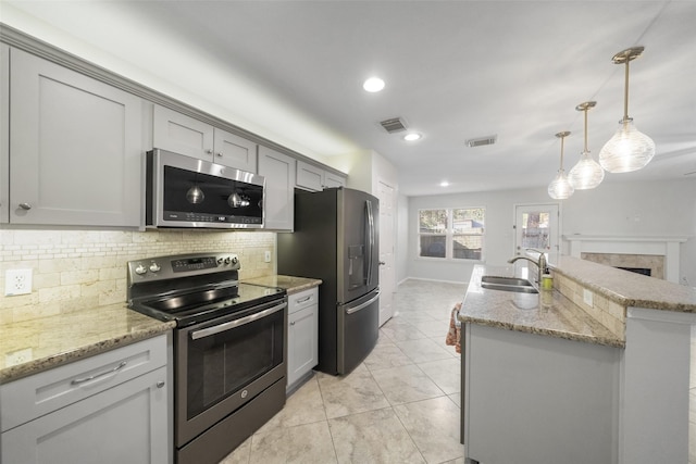 kitchen featuring gray cabinetry, sink, an island with sink, pendant lighting, and appliances with stainless steel finishes