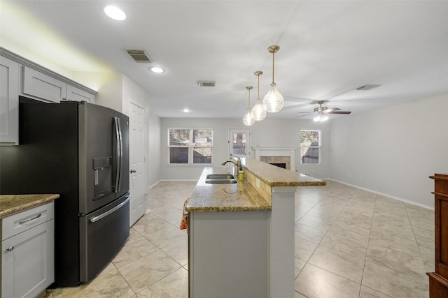 kitchen featuring a kitchen island with sink, sink, ceiling fan, decorative light fixtures, and stainless steel fridge with ice dispenser