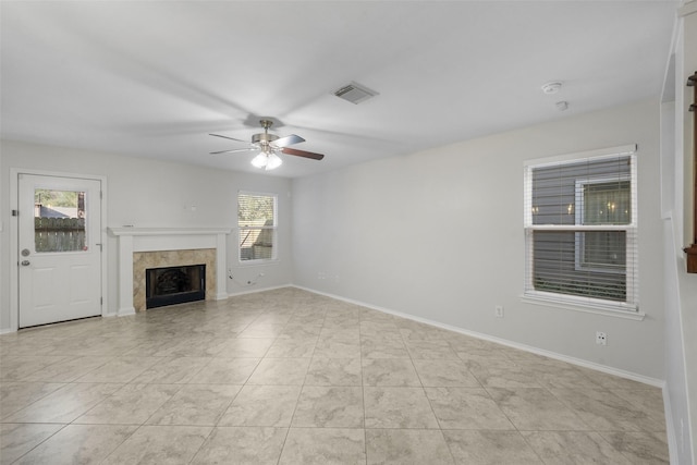 unfurnished living room with ceiling fan, a fireplace, light tile patterned floors, and plenty of natural light