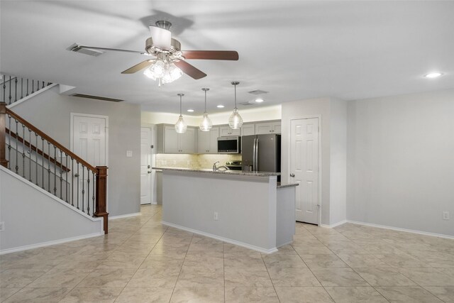 kitchen with light stone counters, ceiling fan, a kitchen island with sink, and appliances with stainless steel finishes