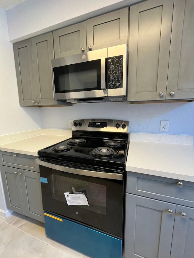 kitchen featuring black electric range, light tile patterned floors, and gray cabinetry