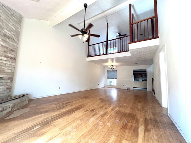 unfurnished living room featuring beam ceiling, ceiling fan with notable chandelier, high vaulted ceiling, and hardwood / wood-style floors