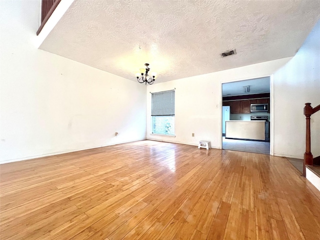 unfurnished living room featuring a chandelier, a textured ceiling, and light wood-type flooring