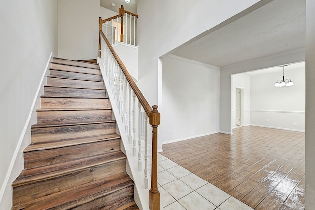 staircase with tile patterned floors, ornamental molding, and a notable chandelier