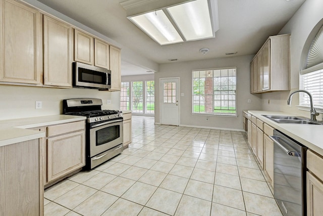 kitchen with light tile patterned floors, light brown cabinetry, sink, and appliances with stainless steel finishes