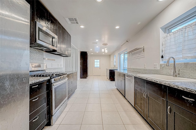 kitchen with backsplash, sink, light stone countertops, light tile patterned floors, and stainless steel appliances