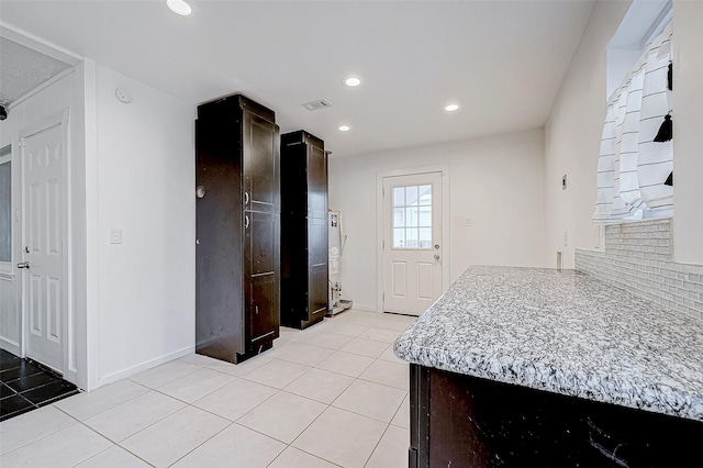 kitchen featuring tasteful backsplash, dark brown cabinetry, light stone countertops, and light tile patterned floors