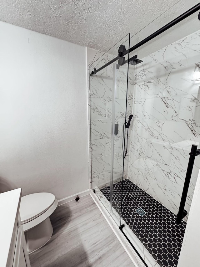 bathroom featuring vanity, a textured ceiling, wood-type flooring, toilet, and a shower with shower door