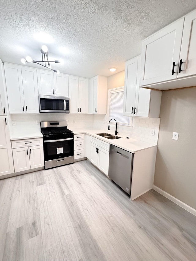 kitchen featuring sink, decorative backsplash, light wood-type flooring, white cabinetry, and stainless steel appliances