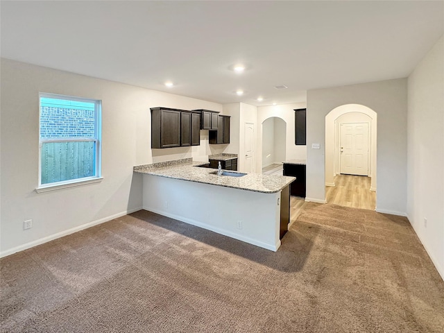 kitchen with kitchen peninsula, light carpet, sink, and light stone counters