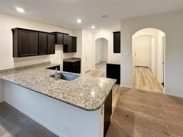 kitchen with kitchen peninsula, light carpet, light stone countertops, and sink