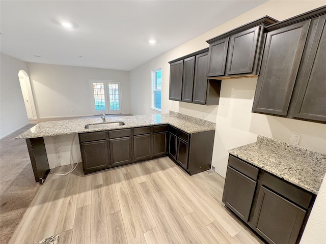 kitchen with sink, light stone counters, light hardwood / wood-style flooring, kitchen peninsula, and dark brown cabinets