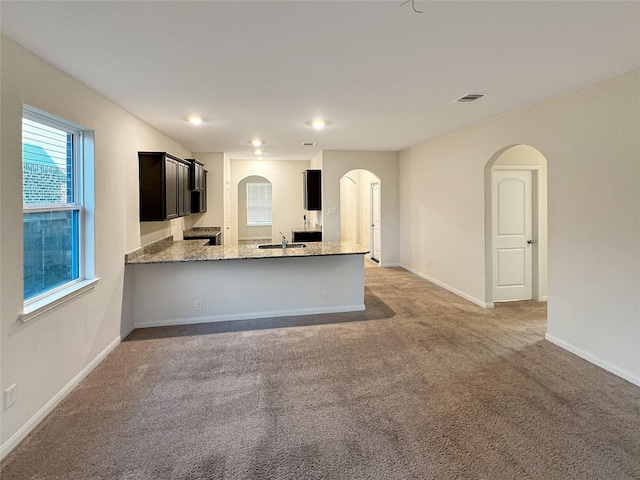 kitchen featuring kitchen peninsula, light colored carpet, light stone counters, and sink