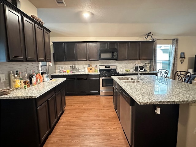 kitchen with sink, stainless steel appliances, backsplash, a center island with sink, and light wood-type flooring