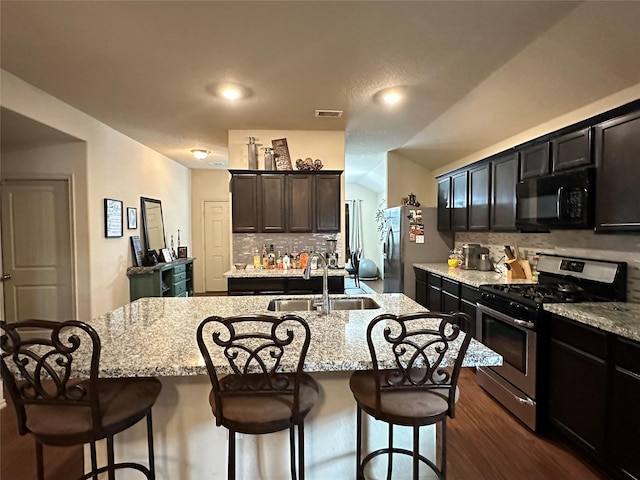 kitchen with a center island with sink, a kitchen breakfast bar, sink, light stone countertops, and stainless steel appliances