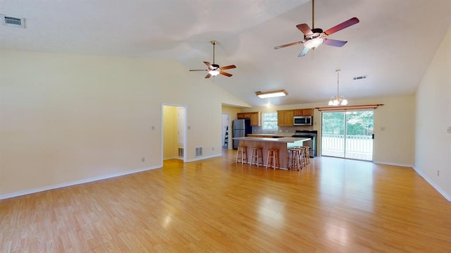 unfurnished living room with ceiling fan with notable chandelier, light hardwood / wood-style floors, and high vaulted ceiling