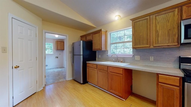 kitchen with sink, light hardwood / wood-style flooring, backsplash, vaulted ceiling, and appliances with stainless steel finishes