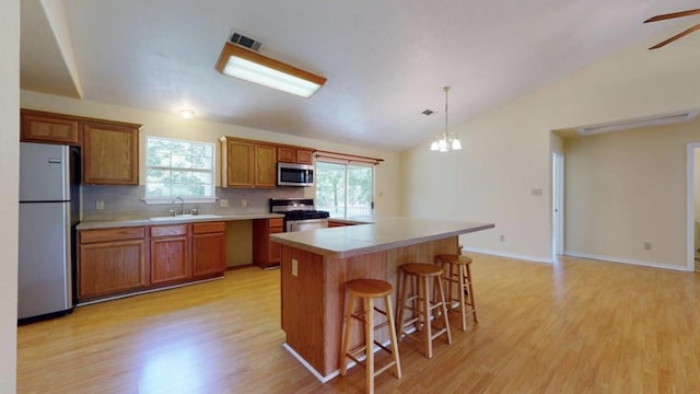 kitchen featuring decorative backsplash, appliances with stainless steel finishes, pendant lighting, light hardwood / wood-style floors, and a kitchen island