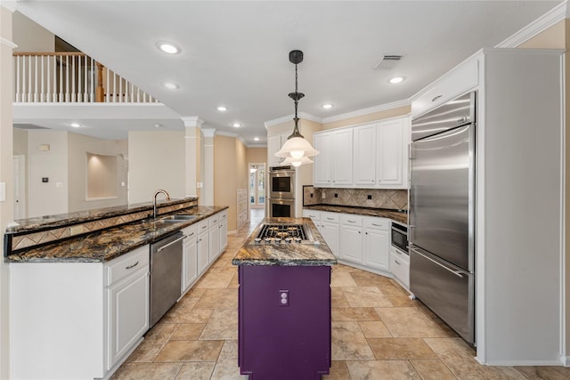 kitchen featuring sink, hanging light fixtures, built in appliances, ornate columns, and white cabinetry