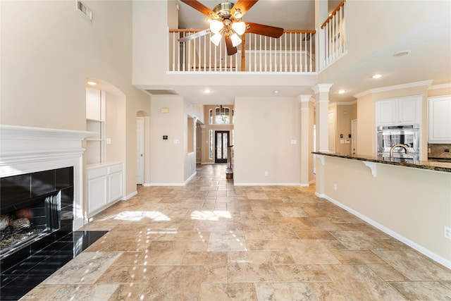 unfurnished living room with ornamental molding, ceiling fan, sink, a tile fireplace, and a high ceiling