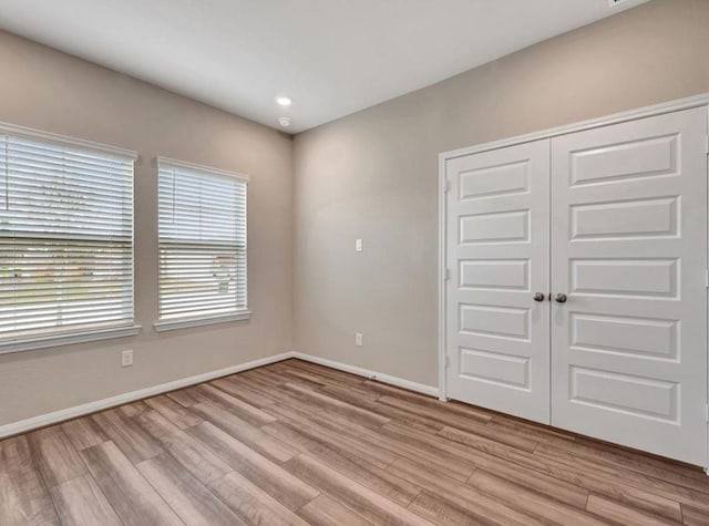 unfurnished bedroom featuring multiple windows, a closet, and light hardwood / wood-style flooring