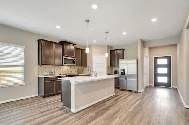 kitchen with backsplash, light wood-type flooring, decorative light fixtures, dark brown cabinets, and stainless steel appliances