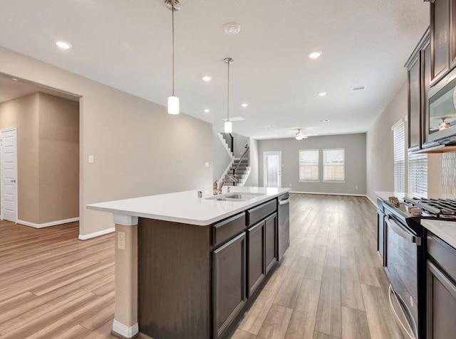 kitchen featuring dark brown cabinets, stainless steel appliances, a kitchen island with sink, sink, and hanging light fixtures