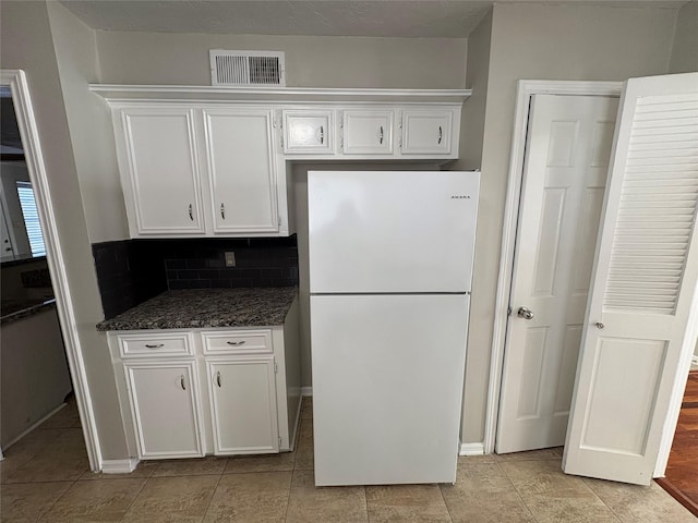 kitchen featuring tasteful backsplash, dark stone countertops, white fridge, white cabinetry, and light tile patterned flooring