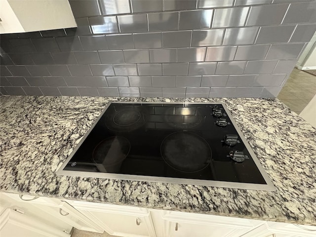 details featuring white cabinets, light stone countertops, and black electric cooktop