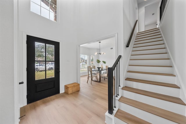 entryway with light hardwood / wood-style flooring, a towering ceiling, and a notable chandelier