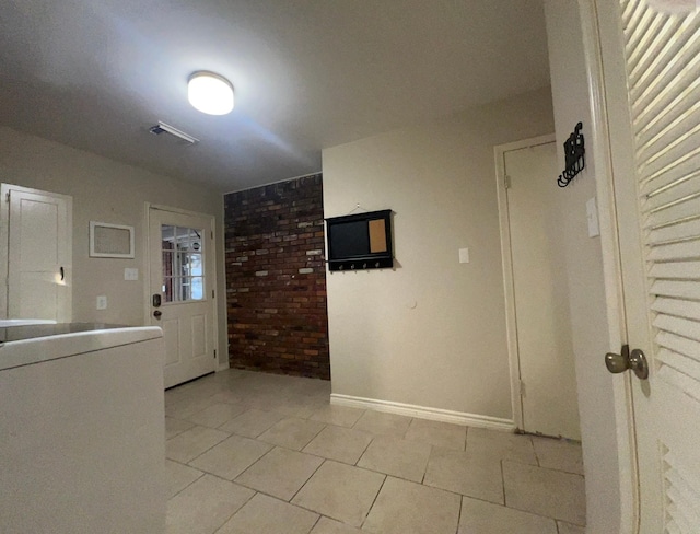 laundry area featuring brick wall and light tile patterned floors