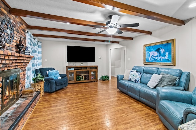 living room featuring a fireplace, light wood-type flooring, ceiling fan, and beam ceiling