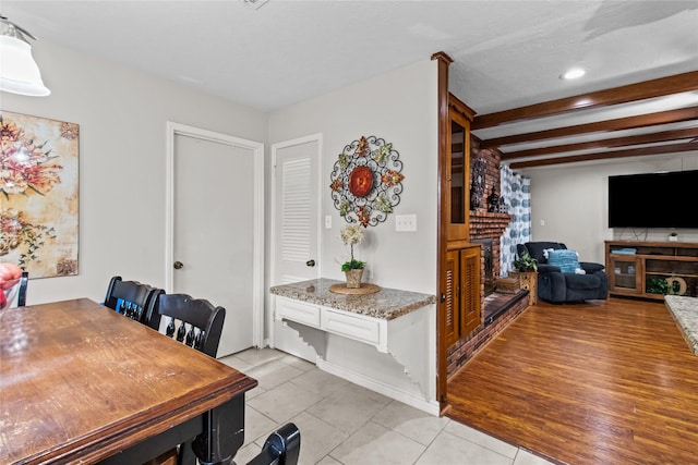 dining space featuring beam ceiling, a brick fireplace, and light tile patterned flooring