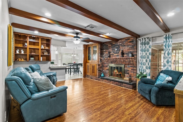 living room featuring a brick fireplace, ceiling fan, hardwood / wood-style flooring, and beamed ceiling