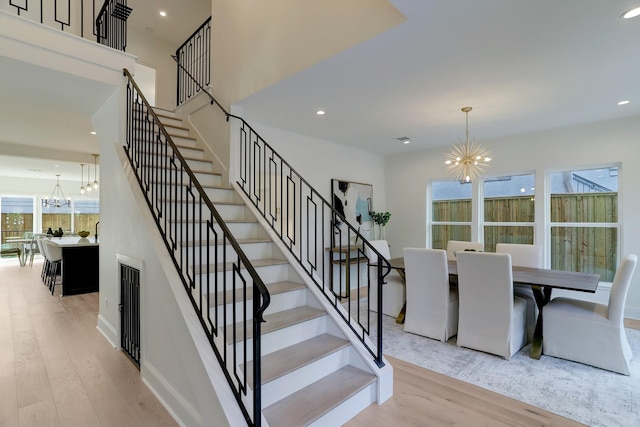 stairs featuring a healthy amount of sunlight, wood-type flooring, and a notable chandelier