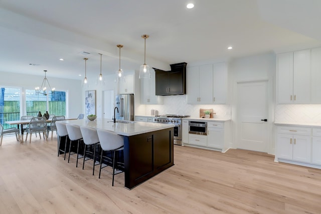 kitchen with a center island with sink, white cabinetry, high quality appliances, and light hardwood / wood-style floors