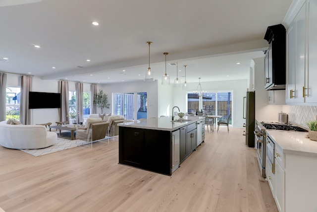 kitchen with a center island with sink, sink, decorative light fixtures, white cabinetry, and stainless steel appliances