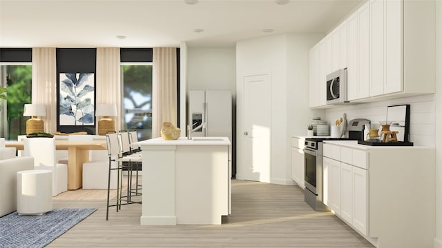 kitchen with stainless steel appliances, a kitchen breakfast bar, light hardwood / wood-style floors, a center island with sink, and white cabinets