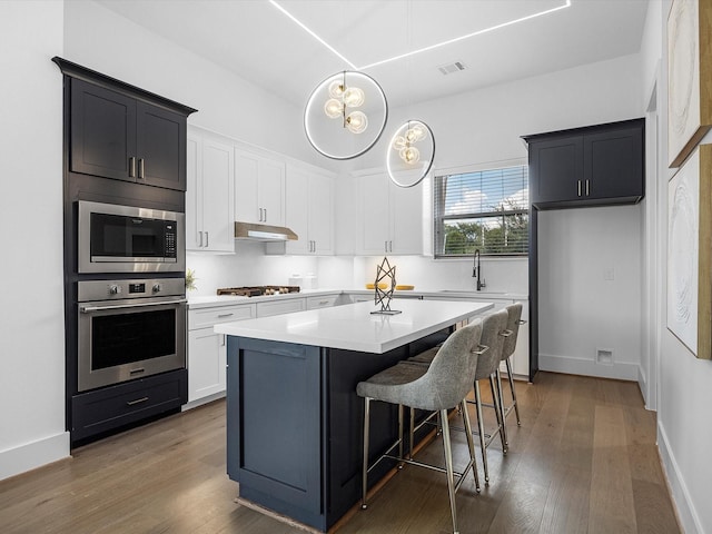 kitchen featuring dark hardwood / wood-style flooring, stainless steel appliances, sink, white cabinets, and a center island