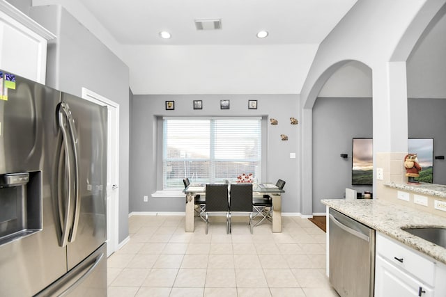 kitchen with vaulted ceiling, light stone countertops, light tile patterned floors, white cabinetry, and stainless steel appliances