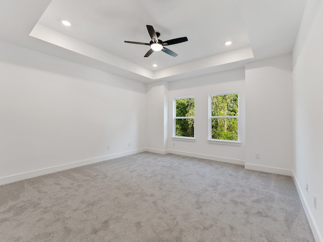 empty room with a raised ceiling, ceiling fan, and light colored carpet