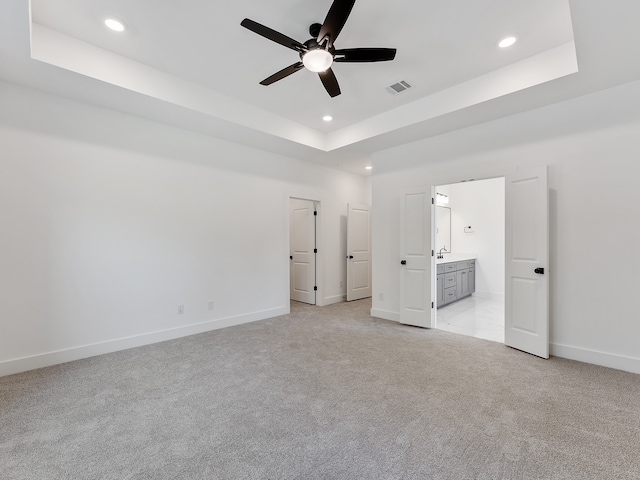 unfurnished bedroom with ceiling fan, ensuite bathroom, light carpet, and a tray ceiling