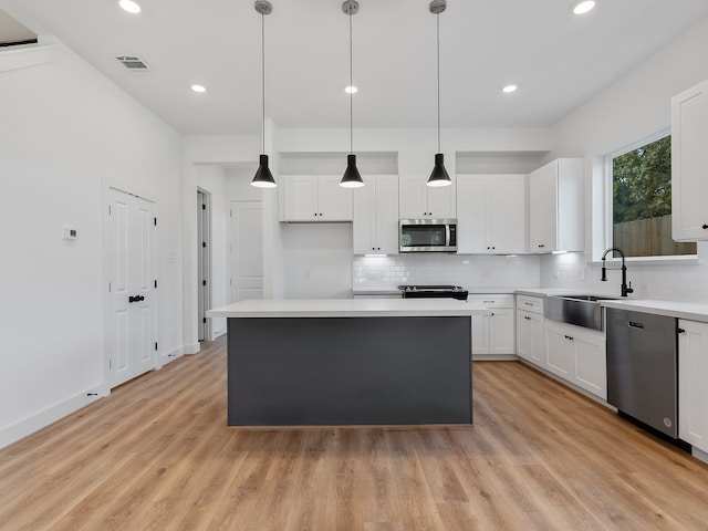 kitchen with white cabinets, decorative light fixtures, a center island, and appliances with stainless steel finishes