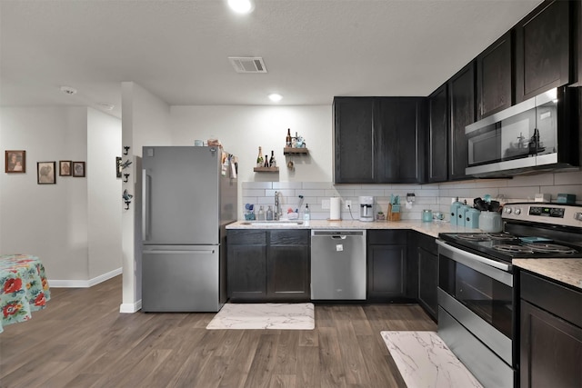 kitchen with sink, backsplash, hardwood / wood-style floors, stainless steel appliances, and light stone counters