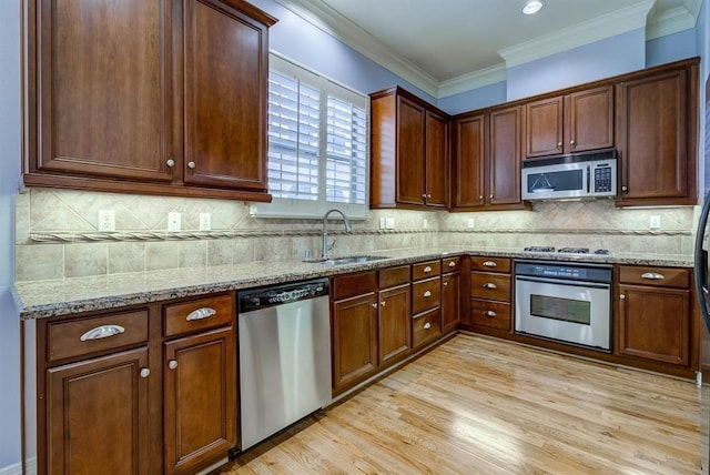 kitchen featuring sink, light stone counters, light hardwood / wood-style floors, decorative backsplash, and appliances with stainless steel finishes