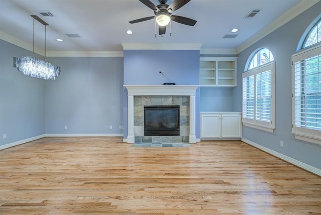 unfurnished living room with a tile fireplace, ceiling fan with notable chandelier, light hardwood / wood-style flooring, built in shelves, and ornamental molding