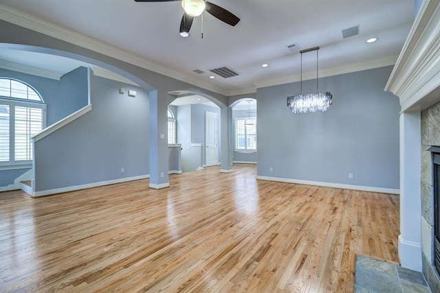 unfurnished living room with ceiling fan with notable chandelier, crown molding, a tile fireplace, and light hardwood / wood-style flooring