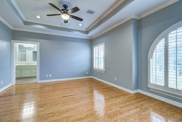 interior space featuring ceiling fan with notable chandelier, a raised ceiling, crown molding, light wood-type flooring, and connected bathroom